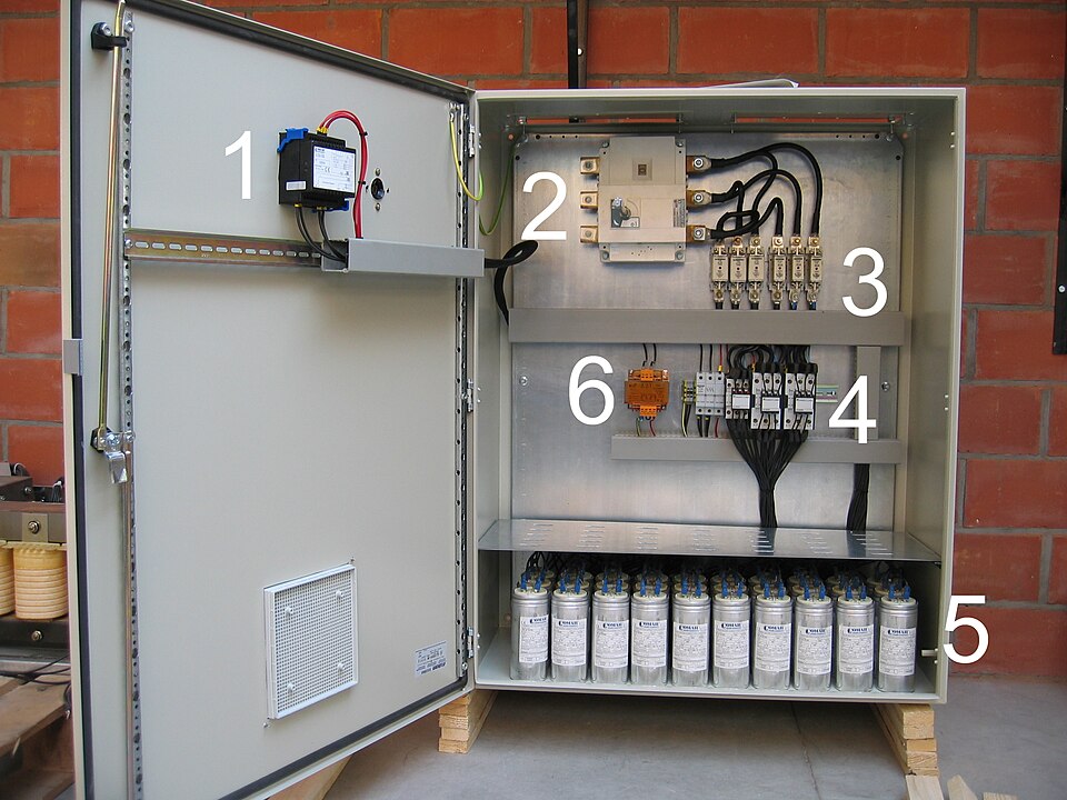 Open 400 V power factor correction capacitor bank (Comar type B35) in a cabinet: regulator, fuses, contactors and capacitor cans numbered.
